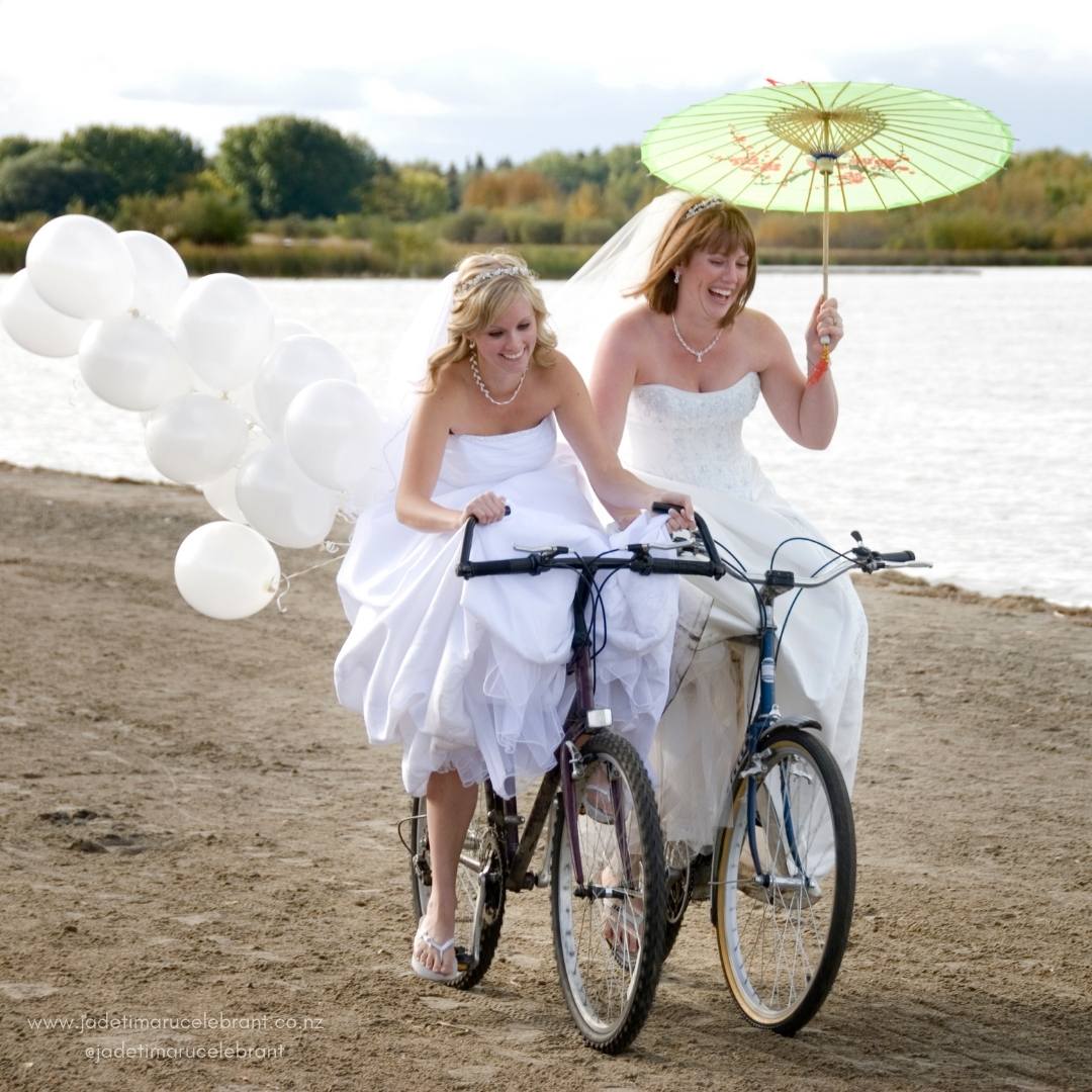 Same-sex couple of two brides just married riding bikes. Jade Whaley Wedding Celebrant, NZ