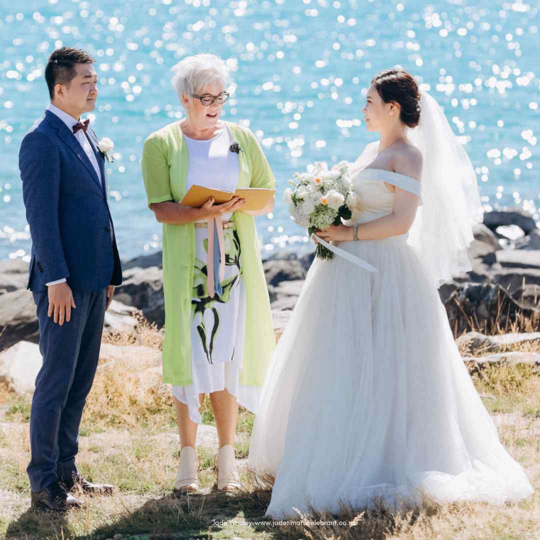 Chinese couple smiling at each other as Jade Whaley, wedding celebrant, marries them at Lake Tekapo. 