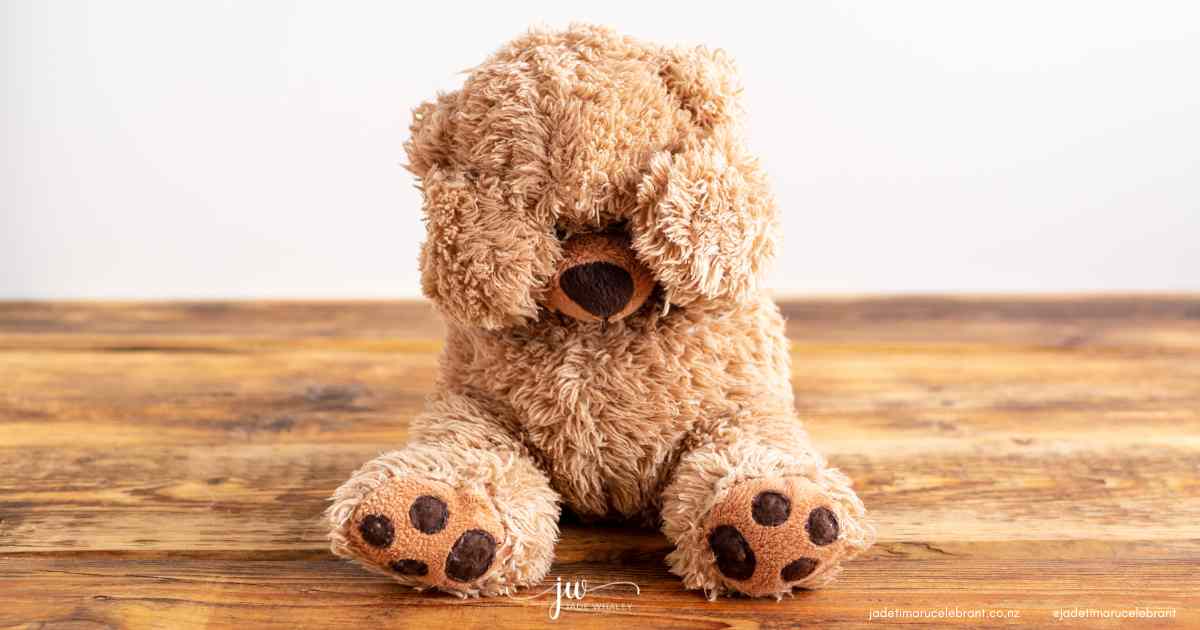 Brown furry teddy bear, sitting on a brown wooden floor with its head down and paws over its eyes. It looks sad. Timaru Funeral Celebrant Jade Whaley, NZ.