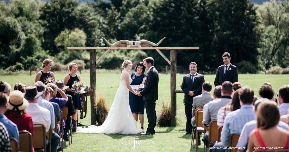 Woman celebrant holding her cermony book so the bride can read her vows to her grow, Setting is on a farm with horns on the archway. jade Whaley Timaru Wedding Celebrant South Canterbury NZ