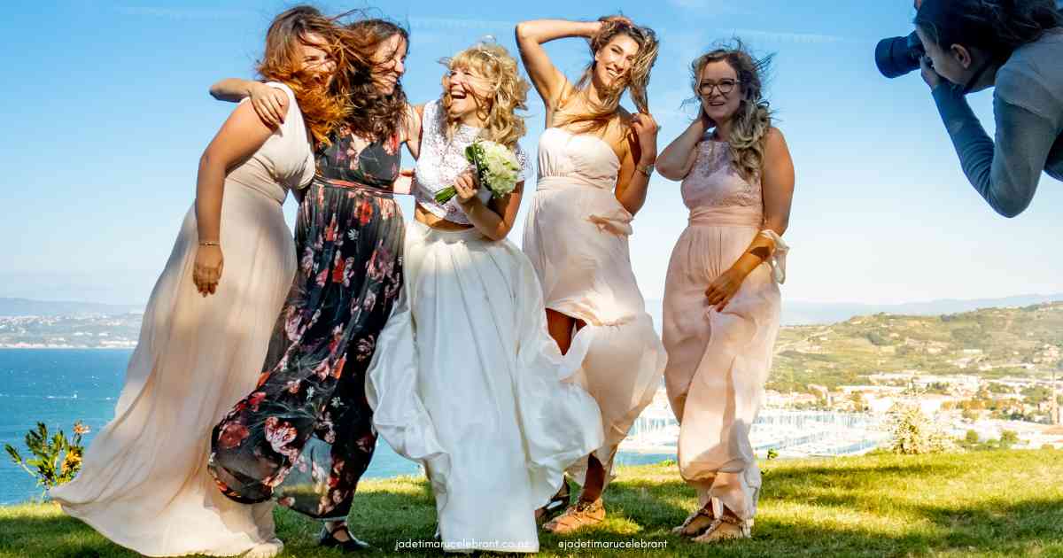 Bride standing with wedding guests and her bridesmaids as the wind blows their hair and dresses. They are having their photo taken from a wedding photographer.