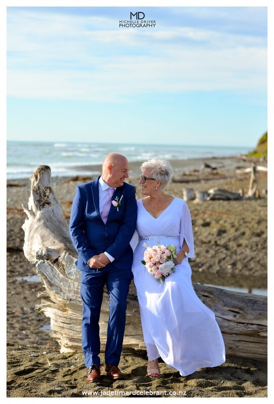 Bride and groom sitting on log smiling at each other at Patiti Point in Timaru.