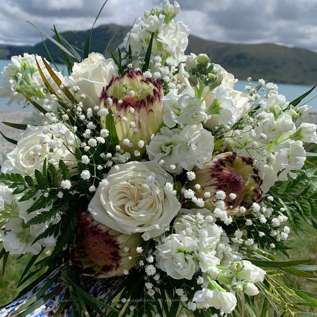Elegant fresh flower wedding bouquet with white flowers, green leaves, and a striking protea.