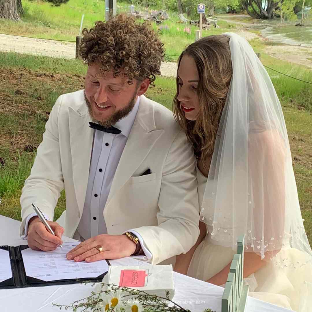 Newly married couple sitting outside signing legal paperwork after eloping at Lake Tekapo, New Zealand.