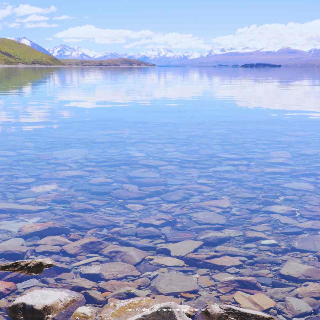 The clear waters of Lake Tekapo, New Zealand, reflect the Southern Alps snow-capped mountains and blue sky. 